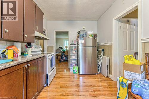 Kitchen area featuring wood-finish flooring, two-tone cabinetry with upper brown and lower wood-tone finishes, a white tile backsplash, and a built-in range - 819 Duke Street, Cambridge, ON - Indoor Photo Showing Kitchen