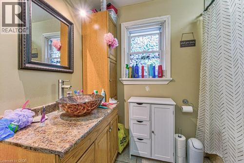 Bathroom featuring a vessel sink with an ornate glass basin, a vanity with a faux-granite countertop and wood-finish cabinetry, a framed mirror, and a wall-mounted storage cabinet - 819 Duke Street, Cambridge, ON - Indoor Photo Showing Bathroom