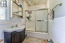 Bathroom featuring a white subway tile shower, sliding glass shower doors, and a vanity with an integrated sink - 