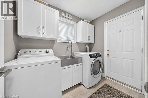 Laundry room featuring white cabinetry, a stainless steel utility sink with a high-arc faucet, and tiled flooring - 30 Carriagegate Drive, Hamilton, ON - Indoor Photo Showing Laundry Room