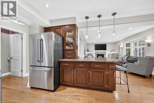 Kitchen island with rich wood cabinetry and a speckled countertop, featuring three pendant lights overhead - 30 Carriagegate Drive, Hamilton, ON - Indoor Photo Showing Kitchen