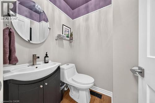Powder room featuring a curved vanity with a white basin, a wall-mounted round mirror, and wood-finish flooring - 30 Carriagegate Drive, Hamilton, ON - Indoor Photo Showing Bathroom