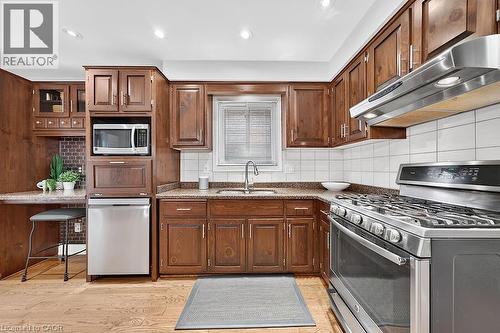 Kitchen featuring wood-finish cabinetry, granite-style countertops, stainless steel appliances, a tile backsplash, and wood-finish flooring - 30 Carriagegate Drive, Hamilton, ON - Indoor Photo Showing Kitchen With Stainless Steel Kitchen With Double Sink