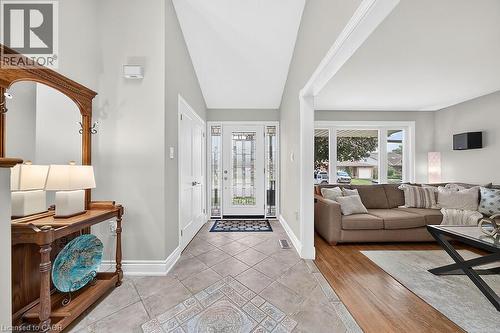 Inviting foyer with tile flooring and a bright glass-paneled entry door, opening to a living area featuring wood-finish flooring and a large window - 30 Carriagegate Drive, Hamilton, ON - Indoor Photo Showing Living Room