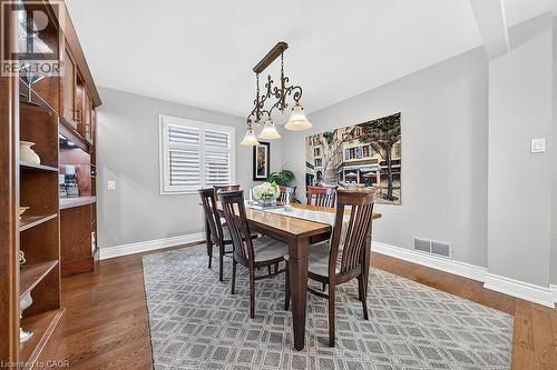 Dining area featuring wood-finish flooring, a built-in wood cabinet with integrated lighting, white baseboards, and a window with white louvered shutters - 30 Carriagegate Drive, Hamilton, ON - Indoor Photo Showing Dining Room