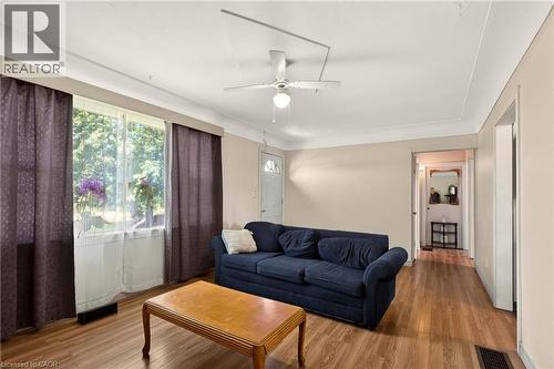 Living area featuring wood-finish flooring, a ceiling fan with integrated lighting, and a large window with sheer and blackout curtain options - 958 Highland Road E, Hamilton, ON 