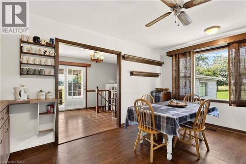 Dining area with wood-finish flooring, a ceiling fan with integrated lighting, and a large window overlooking exterior landscaping - 958 Highland Road E, Hamilton, ON 