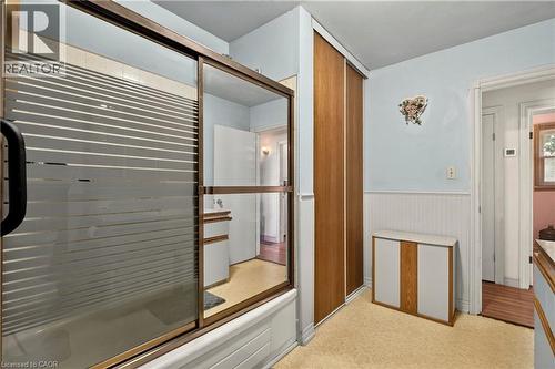 Bathroom featuring a tub with frosted glass sliding doors and bronze-finish trim, wood-paneled closet doors, beadboard wainscoting, and carpet flooring - 958 Highland Road E, Hamilton, ON 