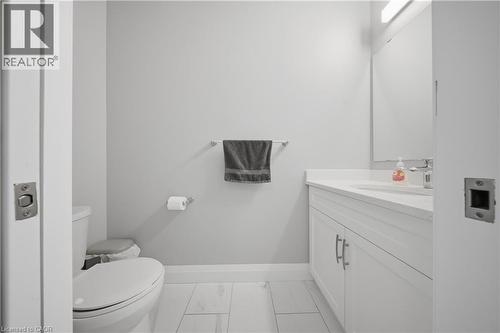 Bathroom featuring light gray walls, white wood-finish flooring, a white vanity with a light-toned countertop, a white toilet, and a wall-mounted mirror - 107 Stephenson Way, Palmerston, ON - Indoor Photo Showing Bathroom