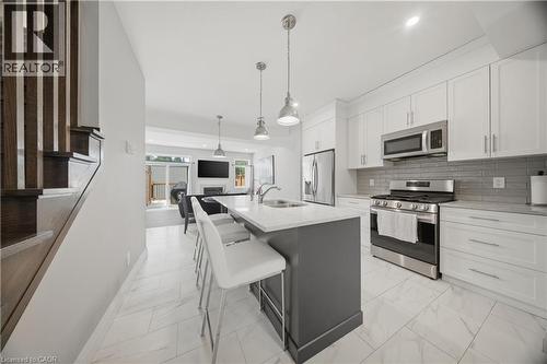 Open-concept kitchen featuring white shaker cabinetry, stainless steel appliances, a grey subway tile backsplash, and a central island with a light-colored countertop - 107 Stephenson Way, Palmerston, ON - Indoor Photo Showing Kitchen With Stainless Steel Kitchen With Double Sink With Upgraded Kitchen