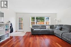 Living area featuring rich wood-finish flooring, white walls, and a large window providing natural light - 