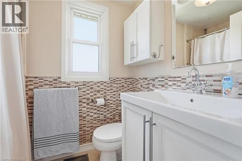 Bathroom featuring a white vanity with integrated sink, chrome faucet, wall-mounted mirror, white wall cabinetry, and a mosaic tile wainscoting - 86 San Remo Drive, Hamilton, ON - Indoor Photo Showing Bathroom