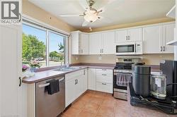 Kitchen featuring white shaker-style cabinetry, a stainless steel dishwasher, a stainless steel gas range, an over-the-range microwave, and a double basin stainless steel sink - 