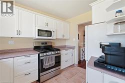Kitchen featuring white shaker-style cabinetry, stainless steel range with overhead microwave, and tile flooring - 
