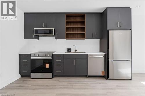 Modern kitchen featuring dark grey cabinetry, light-toned wood-finish flooring, and a full suite of stainless steel appliances including a refrigerator, range, microwave, and dishwasher - 146 Everett Common, St. Catharines, ON - Indoor Photo Showing Kitchen
