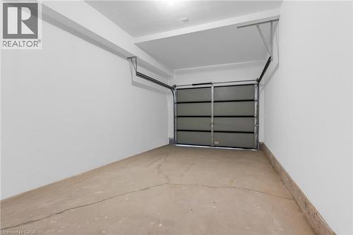 Single-car garage featuring a sectional overhead door with upper window panels, concrete flooring, white painted walls, and overhead lighting - 146 Everett Common, St. Catharines, ON - Indoor Photo Showing Garage