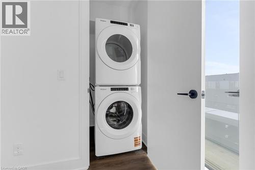 Compact laundry closet featuring a stacked white washer and dryer unit, dark wood-finish flooring, and a white interior door with matte black hardware - 146 Everett Common, St. Catharines, ON - Indoor Photo Showing Laundry Room