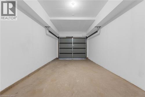 Spacious garage featuring a light gray sectional garage door, smooth concrete flooring, and white painted walls - 146 Everett Common, St. Catharines, ON - Indoor Photo Showing Garage