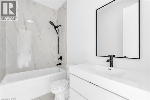 Bathroom featuring a white bathtub with a matte black shower head and faucet, marble-look tiled shower surround, white toilet, and a vanity with an integrated sink and matte black faucet - 146 Everett Common, St. Catharines, ON - Indoor Photo Showing Bathroom