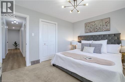 Carpeted bedroom with a bi-fold closet, contemporary chandelier, and a hallway featuring wood-finish flooring - 60 Lysanda Avenue, London, ON - Indoor Photo Showing Bedroom