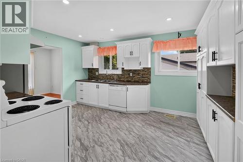 Bright kitchen featuring white cabinetry with dark hardware, stone-finish countertops, a mosaic tile backsplash, and wood-finish flooring - 186 Glenmor Drive, Caledonia, ON - Indoor Photo Showing Kitchen