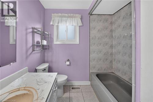 Bathroom featuring a single vanity with a patterned countertop, a white toilet, a frosted window, and a bathtub with tiled surround - 186 Glenmor Drive, Caledonia, ON - Indoor Photo Showing Bathroom