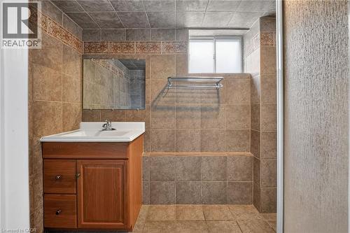 Bathroom featuring tiled walls, a wood-finish vanity with an integrated sink, a wall-mounted mirror, a tiled shower area, and a privacy window - 186 Glenmor Drive, Caledonia, ON - Indoor Photo Showing Bathroom