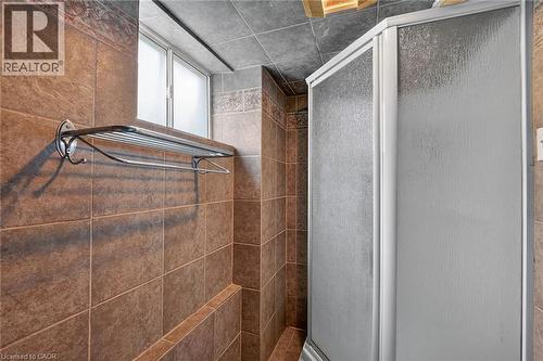 Shower enclosure with textured glass panels, surrounded by earth-toned wall tiling and a decorative border - 186 Glenmor Drive, Caledonia, ON - Indoor Photo Showing Bathroom