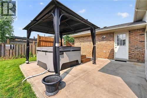 Poured concrete patio featuring an outdoor spa with a black gazebo, brick exterior, and a white paneled door with window inserts - 186 Glenmor Drive, Caledonia, ON - Outdoor With Exterior