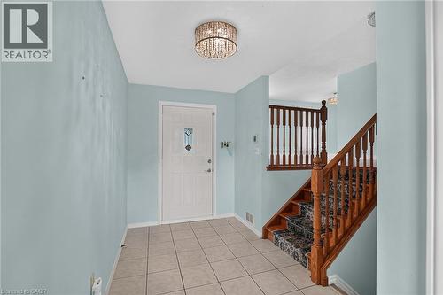 Tiled entryway with a decorative flush mount light fixture, paneled entry door with an arched stained glass insert, and a wooden staircase featuring patterned risers and balusters - 186 Glenmor Drive, Caledonia, ON - Indoor Photo Showing Other Room
