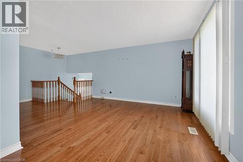 Expansive room featuring wood-finish flooring, light blue wall paint, white baseboards, and a wooden staircase with balusters - 186 Glenmor Drive, Caledonia, ON - Indoor Photo Showing Other Room