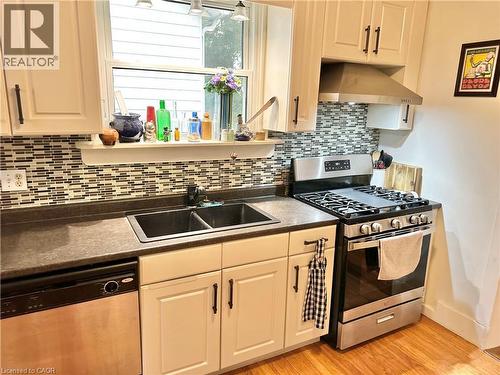Kitchen featuring shaker-style cabinetry, mosaic tile backsplash, double basin sink, stainless steel appliances, and wood-finish flooring - 88 Brook Street, Simcoe, ON - Indoor Photo Showing Kitchen With Double Sink