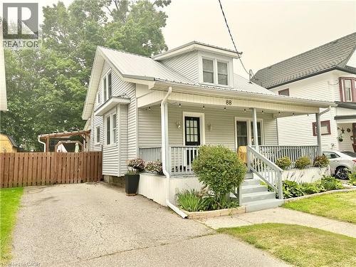 Charming light-colored siding home featuring a covered front porch with railings, a metal roof, and a black front door - 88 Brook Street, Simcoe, ON - Outdoor With Deck Patio Veranda
