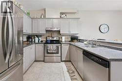 U-shaped kitchen featuring light gray cabinetry, stainless steel appliances, dark speckled countertops, a double basin sink, and tile flooring - 