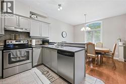 Modern kitchen featuring light gray cabinetry, stainless steel appliances, dark countertops, and tile flooring - 