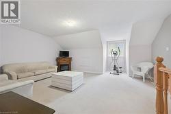 Spacious bonus room featuring sloped ceilings, light carpeting, a built-in electric fireplace with wood mantel, a large window, and a wood banister - 