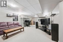 Carpeted recreation room featuring a drop ceiling with recessed lighting and a wall-mounted shelving unit - 