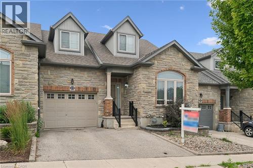 Stone facade townhome featuring a single-car garage with a paneled door, arched window, and dormer windows on the upper level - 23 Knack Lane, Cambridge, ON - Outdoor With Facade