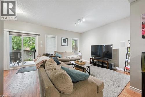 Spacious living area featuring wood-finish flooring, light grey walls, track lighting, and a sliding glass door opening to an outdoor patio with a wooden privacy fence - 23 Knack Lane, Cambridge, ON - Indoor Photo Showing Living Room