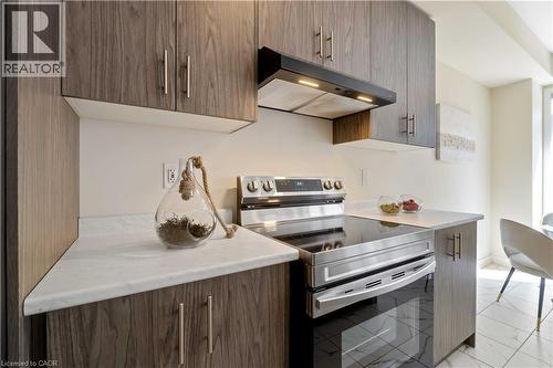 Modern kitchen featuring wood-finish cabinetry, white countertops, stainless steel range with a smooth cooktop, and a coordinating range hood - 10 Lemon Avenue, Thorold, ON - Indoor Photo Showing Kitchen