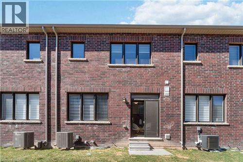 Rear brick facade featuring multiple windows with dark frames, a ground-level patio door, exterior lighting, and a partial grassy area - 10 Lemon Avenue, Thorold, ON - Outdoor With Exterior