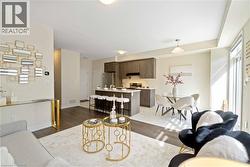 Open-concept living area featuring wood-finish flooring, a contemporary kitchen with a central island and stainless steel appliances, and a dining area with a modern chandelier - 
