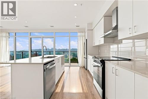 Open-concept kitchen with expansive floor-to-ceiling windows, a large center island featuring an undermount sink and stainless steel dishwasher, wood-finish flooring, and a full suite of stainless ste - 50 Grand Avenue S Unit# 713, Cambridge, ON - Indoor Photo Showing Kitchen With Upgraded Kitchen