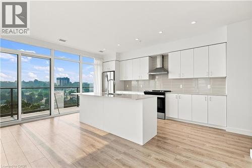 Contemporary kitchen featuring a large central island with an undermount sink, white flat-panel cabinetry, light wood-finish flooring, and a stainless steel appliance suite - 50 Grand Avenue S Unit# 713, Cambridge, ON - Indoor Photo Showing Kitchen With Upgraded Kitchen