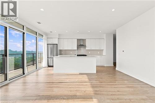 Open concept living area featuring wood-finish flooring, a contemporary kitchen, and expansive sliding glass doors leading to a balcony - 50 Grand Avenue S Unit# 713, Cambridge, ON - Indoor Photo Showing Kitchen