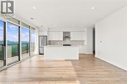 Open concept living area featuring wood-finish flooring, a contemporary kitchen, and expansive sliding glass doors leading to a balcony - 