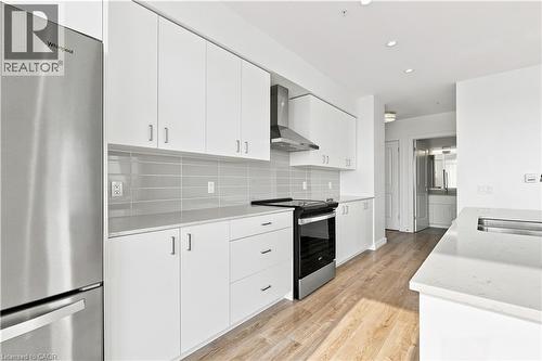 Modern kitchen featuring stainless steel appliances, light wood-finish flooring, white flat-panel cabinetry, light gray subway tile backsplash, and white countertops - 50 Grand Avenue S Unit# 713, Cambridge, ON - Indoor Photo Showing Kitchen With Upgraded Kitchen
