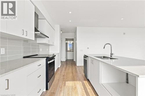 Modern kitchen featuring white cabinetry, light wood-finish flooring, stainless steel appliances, a light-toned backsplash, and recessed lighting - 50 Grand Avenue S Unit# 713, Cambridge, ON - Indoor Photo Showing Kitchen With Double Sink With Upgraded Kitchen