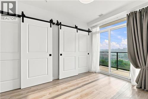 Two white barn doors with black hardware, wood-finish flooring, and a sliding glass door leading to a balcony with a black railing - 50 Grand Avenue S Unit# 713, Cambridge, ON - Indoor Photo Showing Other Room