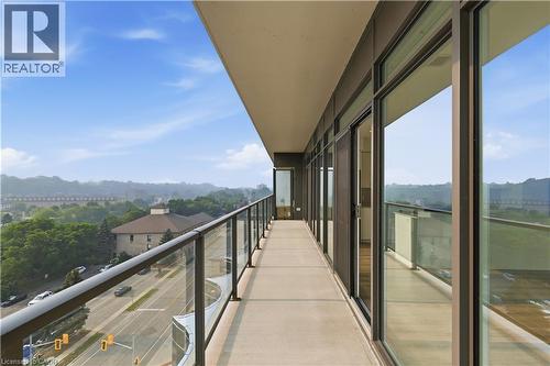 Expansive concrete balcony featuring a full-length glass railing, multiple sliding glass doors, and a partial outdoor ceiling - 50 Grand Avenue S Unit# 713, Cambridge, ON - Outdoor With View With Exterior